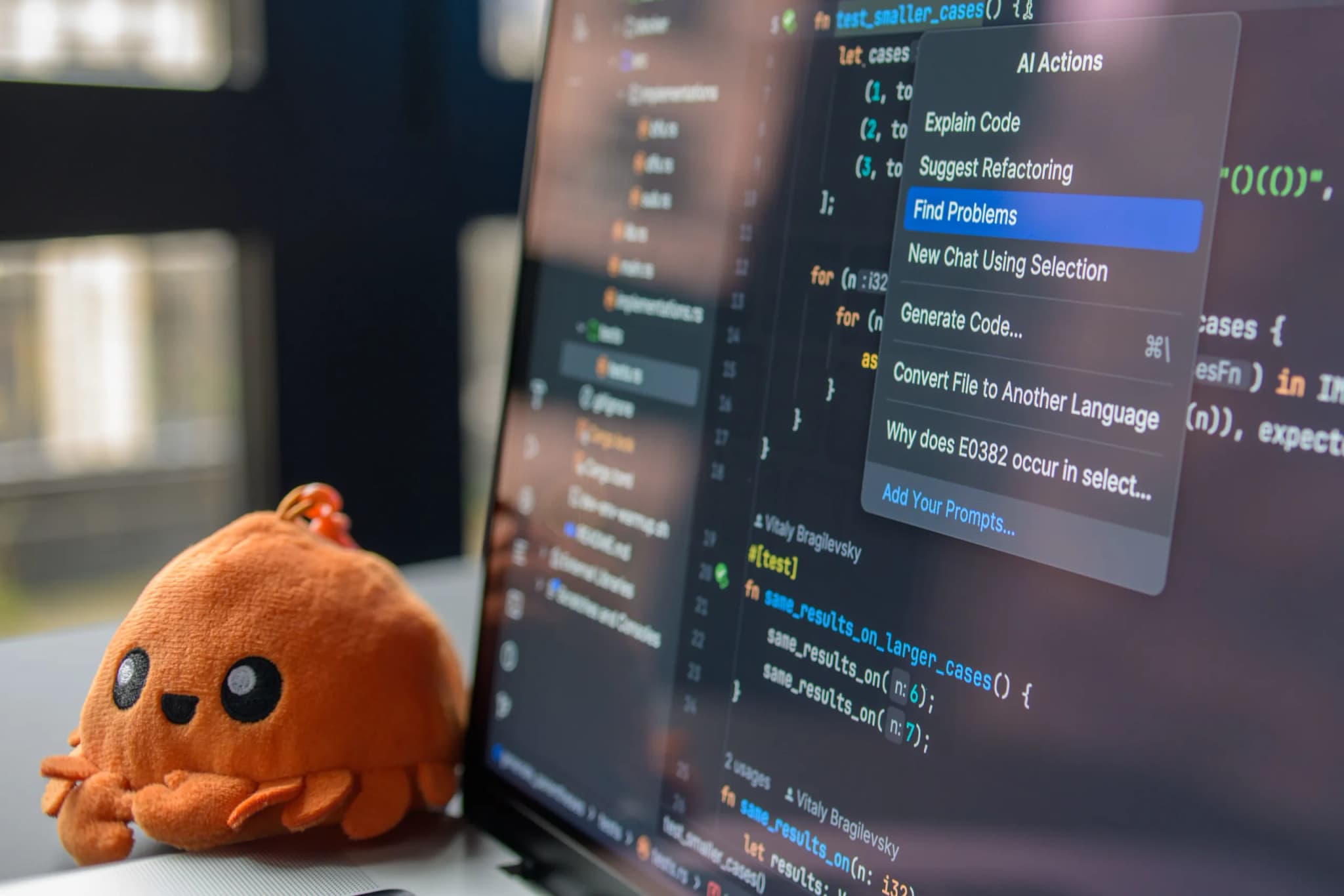 A laptop screen showing source code with an AI actions menu open over it, a small toy sitting beside the display.
