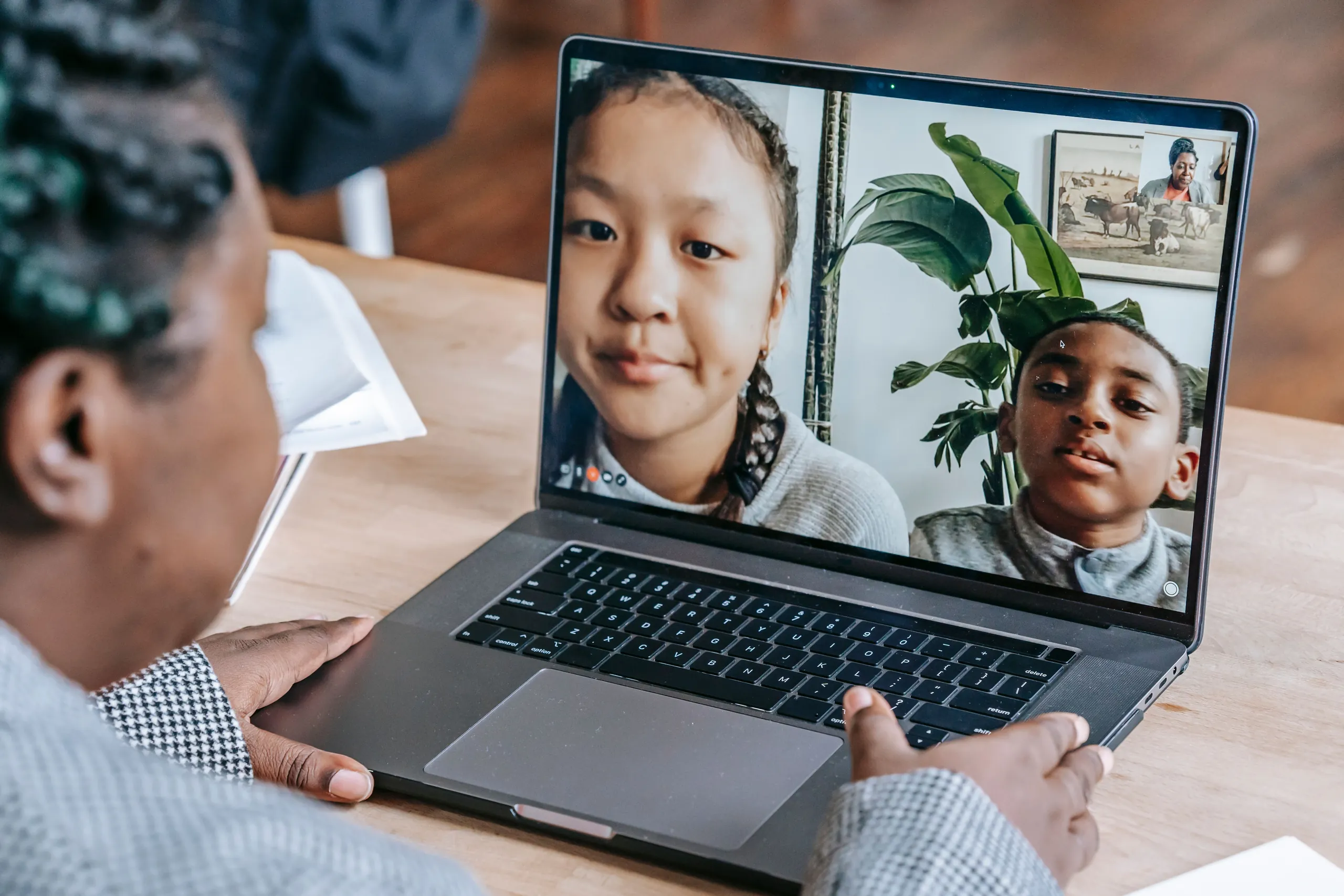 Over-the-shoulder view of someone at a laptop on a video call with two children on screen.