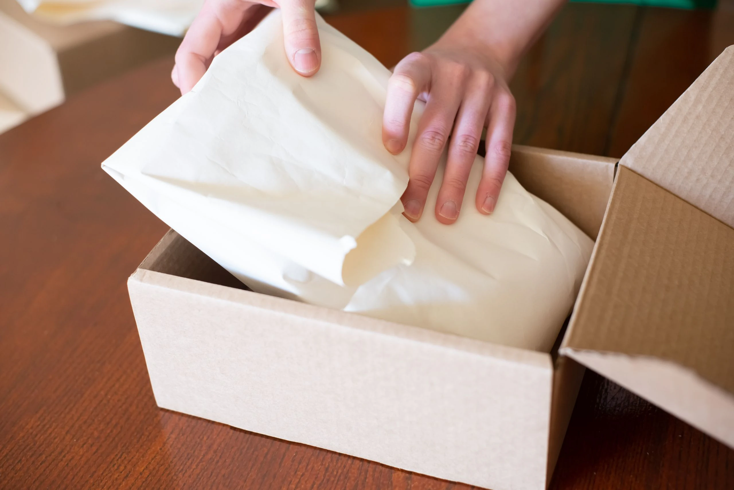 Hands packing an order into a cardboard box.